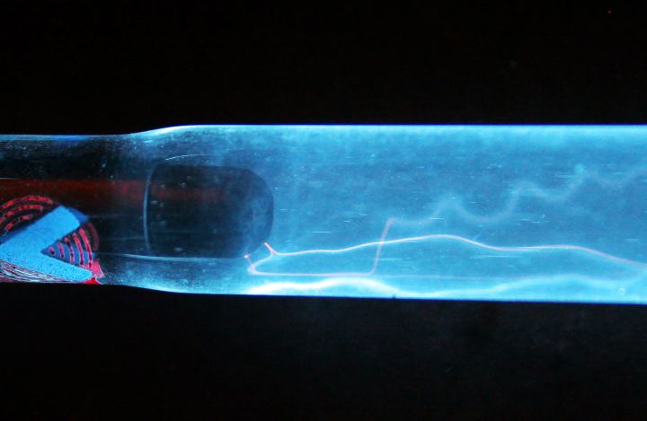 Filamentary discharges in a krypton long-arc lamp

The application of a high voltage at low current across the terminals of flash tubes results in the formation of a filamentary discharge which wanders inside the lamp volume. This discharge is characterized by a very thin plasma channel caused primarily by a fill pressure that is greater than a tenth of an atmosphere. If the lamp is driven with an alternating current, then the discharge filament is more likely to quickly jump position and path upon polarity reversal, which to the naked eye gives the impression that multiple discharges exist at the same time.

Here the plasma is generated inside a krypton-filled pulsed lamp driven with a 15 kV HF power supply operating at 30 kHz. There are several interesting phenomena that are visible in the picture above, such a discharge light emission which is particularly rich in red, a characteristic of krypton (xenon has a much cooler light color). The overall blue color of the tube is from the fluorescence of the trivalent cerium ion which is used as a quartz dopant to absorb UVs. Finally, it is interesting to note that the filamentary discharge often sticks to the wall. There are several reasons for that, such as the enhancement of the local electric field at the glass-gas interface due to the abrupt change in dielectric permittivity there, the emission of photoelectrons by the glass material, and the trapping and release of surface charges. Also, strong radial displacement currents, caused especially by the high operating frequency (i.e., high dV/dt) and by quartz's high relative dielectric constant (3.7-3.8), results in an effective capacitive coupling between the filamentary discharge and the grounded surroundings, which pulls the plasma towards the wall.

It is possible to get multiple filamentary discharges to exist at the same time in such lamp, but this requires some very specific operating conditions, such as a very low drive current in order to get a very high plasma impedance. An other way is to drive the lamp at high frequency in the so-called "single-electrode" mode where only one electrode is connected to the power supply while the opposite electrode is the grounded surrounding. In that case the dynamic positive (capacitive) impedance of the glass wall of the lamp counters the negative (ohmic) one of the plasma, enabling the discharge current distribution to be spread out over multiple locations. In such regime the quartz wall effectively works as a distributed ballasting impedance. The lamp shown here was not driven this way as both electrodes were connected to the HV power supply.


Keywords: Miscellaneous